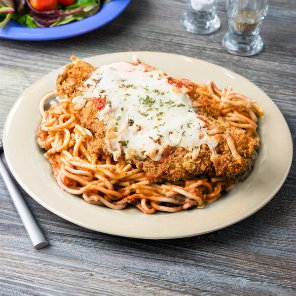 A Diamond Ivory melamine plate with cheese and pasta, chicken, salad, and tomatoes on a table.