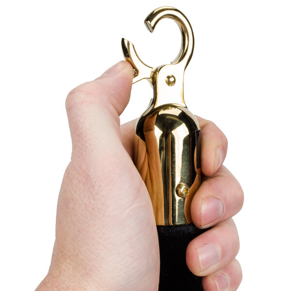 A hand holding a black Aarco stanchion rope with gold brass ends.