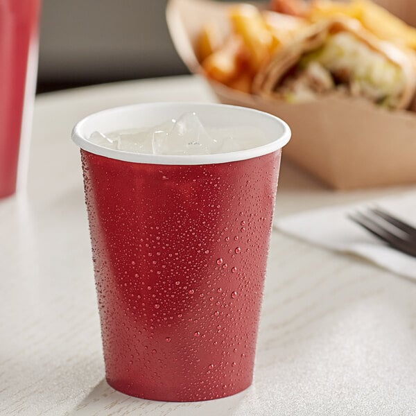 A Creative Converting burgundy paper cup with ice and a straw on a table.