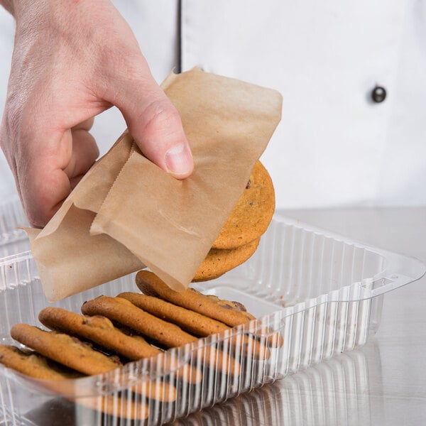 A hand using Bagcraft EcoCraft Bakery Tissue to put a brown paper bag over a cookie in a plastic container.