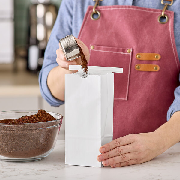 A white paper coffee bag with a reclosable tin tie being filled with ground coffee.