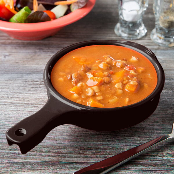 A brown melamine bowl with a handle filled with soup on a table.