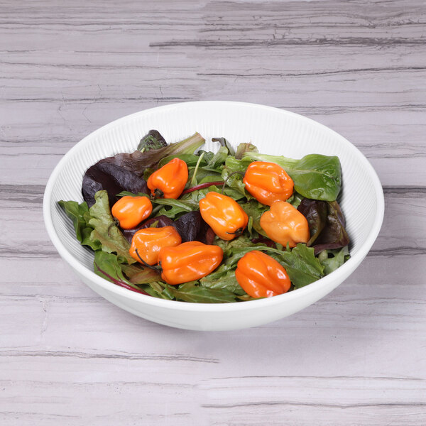 A white Elite Global Solutions melamine bowl filled with salad on a wood table.