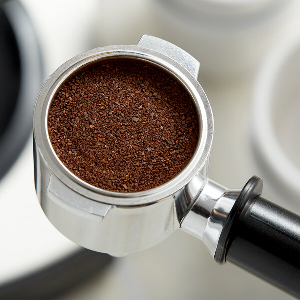 A coffee grinder with Crown Beverages Emperor's Blend coffee beans in it.