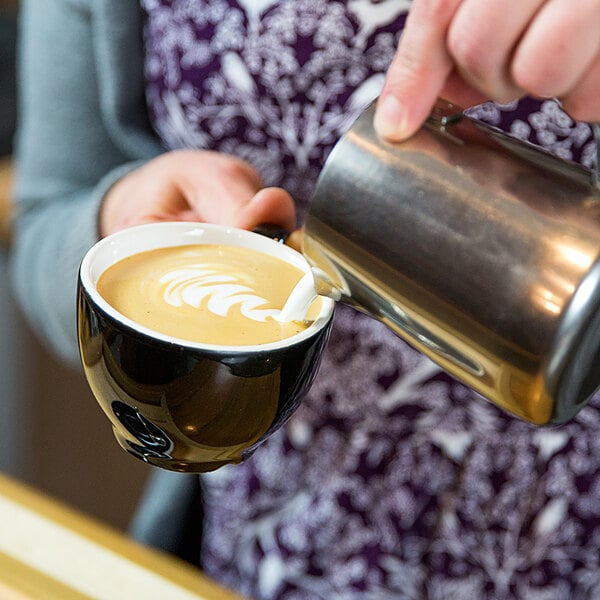 A person pouring Crown Beverages Emperor's Blend ground espresso into a cup of coffee.