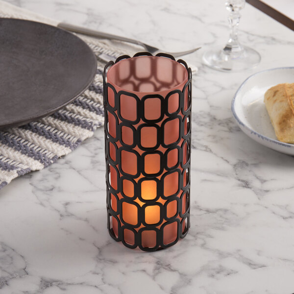 A Sterno black square wire metal candle holder on a table with a lit candle.