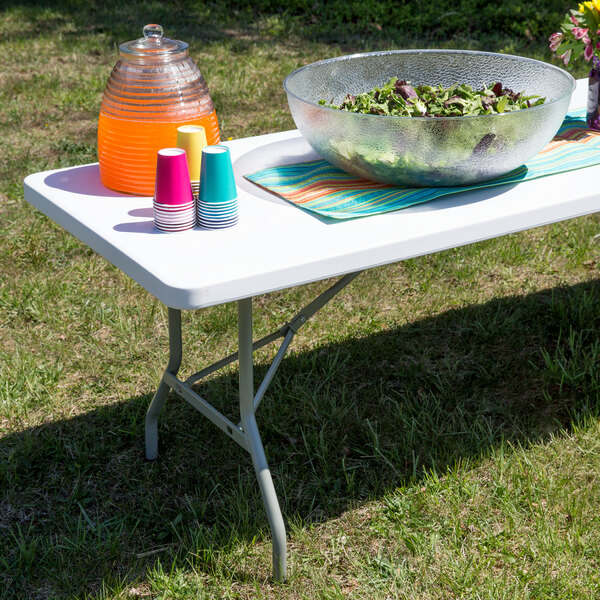 A white Flash Furniture folding table set up with a bowl of salad and a bowl of fruit on it.