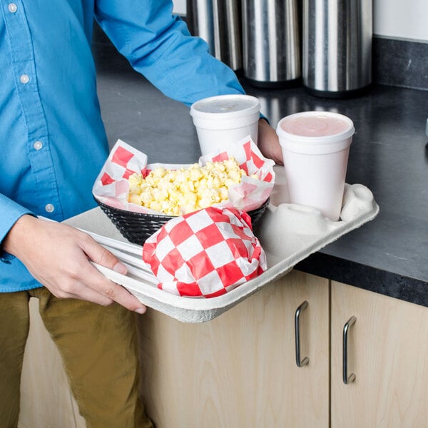 A man holding a Huhtamaki Chinet 2 cup carrier with a white cup and lid.