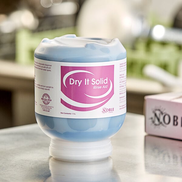 A white and blue Noble Chemical Dry It Solid container on a counter.