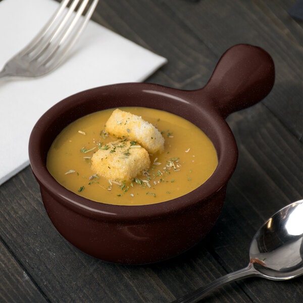 A Tablecraft midnight speckle cast aluminum soup bowl with a handle filled with soup and croutons on a table with a spoon and fork.