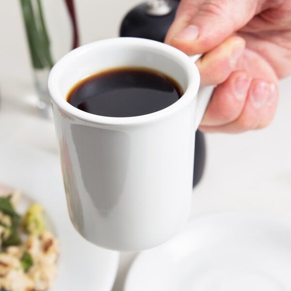 A person holding a Tuxton Alaska bright white china mug filled with coffee over a table with food.