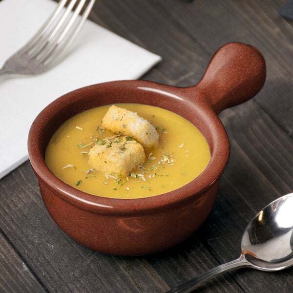 A Tablecraft maroon speckle cast aluminum soup bowl with croutons and a spoon next to it.