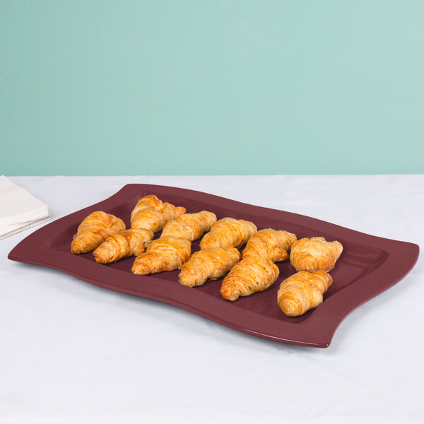 A Maroon speckled rectangular platter with croissants on a table.