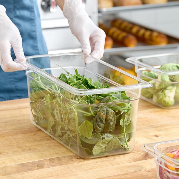 A person using a Cambro clear plastic food pan to hold spinach leaves.