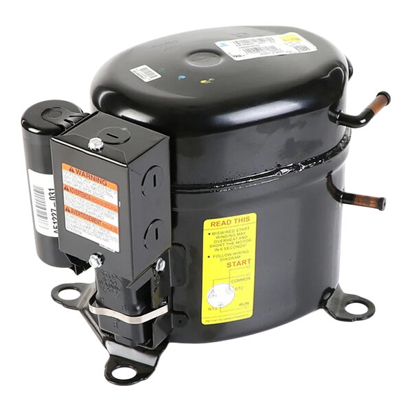 A black cylindrical mechanical component with attached electrical parts, warning labels, and copper tubing connections, likely a refrigeration compressor.