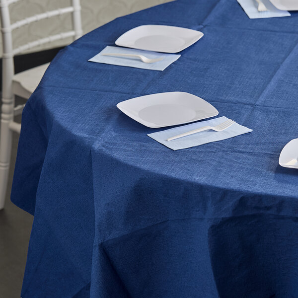 A table with white plates and forks on a navy blue tablecloth.