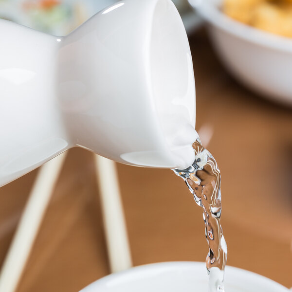 A white jug pouring water into a white GET Porcelain Fuji Sake Bottle.