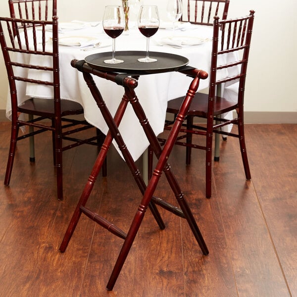 A mahogany wood Tablecraft tray stand with a tray of wine glasses on it.