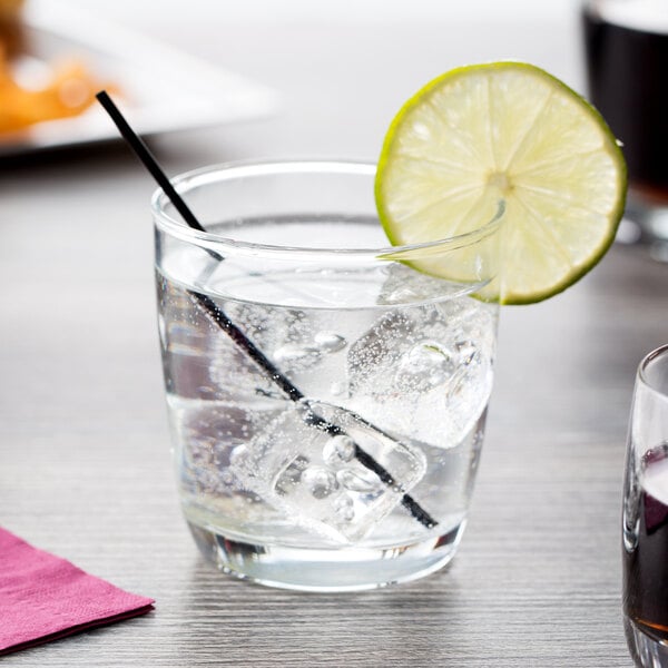 A glass of water with ice, a straw, and a lime slice in an Arcoroc Excalibur Rocks Glass.