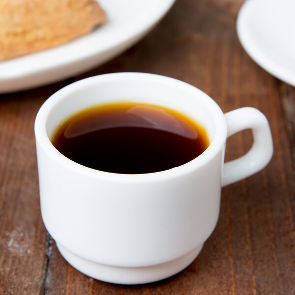 A white Arcoroc cup of coffee on a wooden table.