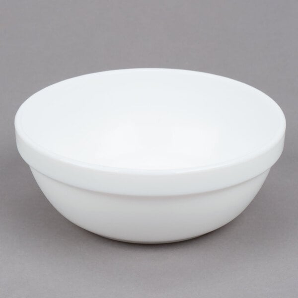 An Arcoroc white stacking bowl on a gray surface.