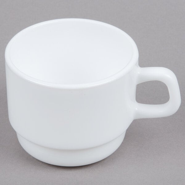 An Arcoroc white coffee cup with a white handle on a grey surface.