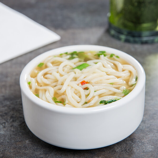 A Tuxton white china bowl filled with noodle soup topped with a green leaf.
