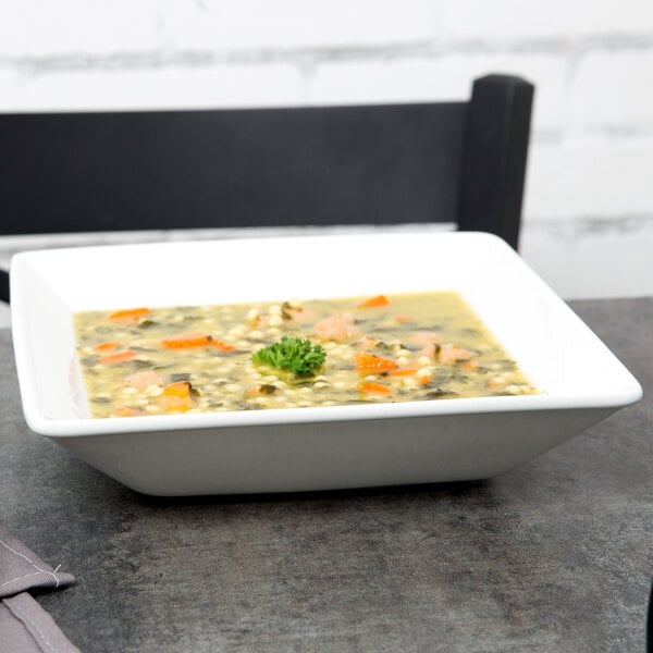 A Tuxton bright white square china bowl filled with soup and vegetables on a table.