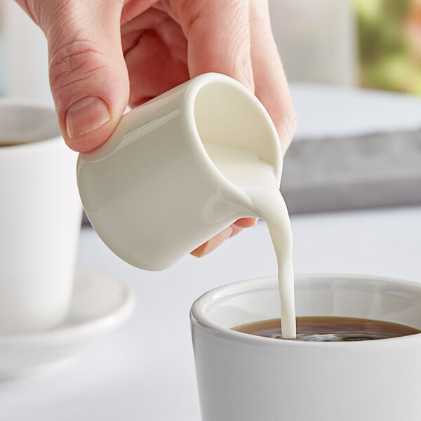 A person pouring milk into a Tuxton eggshell china creamer.
