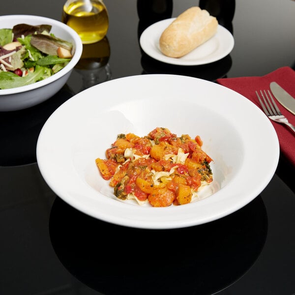 A Tuxton porcelain white pasta bowl filled with pasta and vegetables on a table.