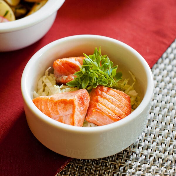 A Tuxton eggshell china bowl with food including salmon, rice, and greens.