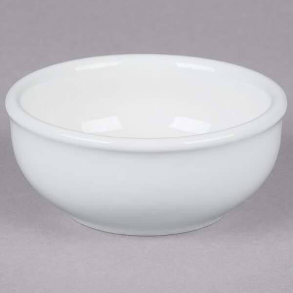 A white Tuxton China sauce dish on a gray surface.