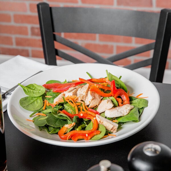 A Tuxton white china pasta bowl filled with salad with chicken and vegetables on a table.