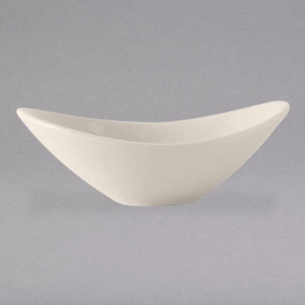 A close-up of a Tuxton oval eggshell white china bowl with a curved edge.