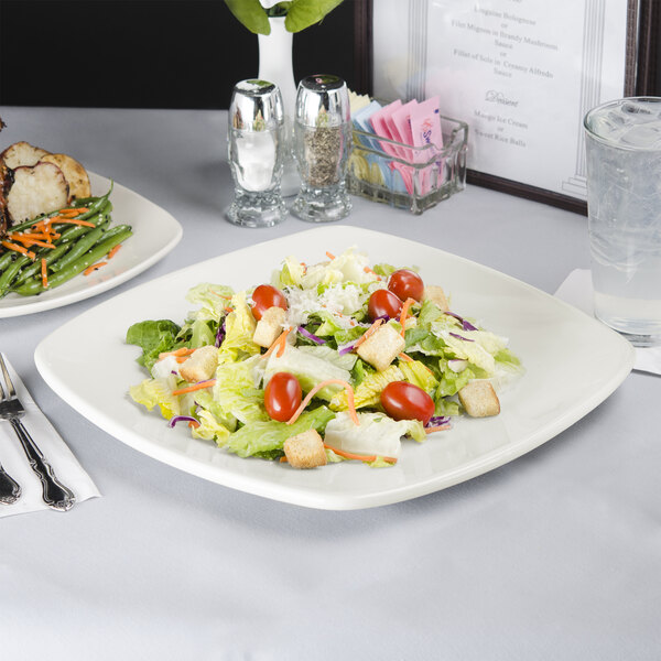 A Tuxton white square china plate with salad on it on a table with a glass of water.