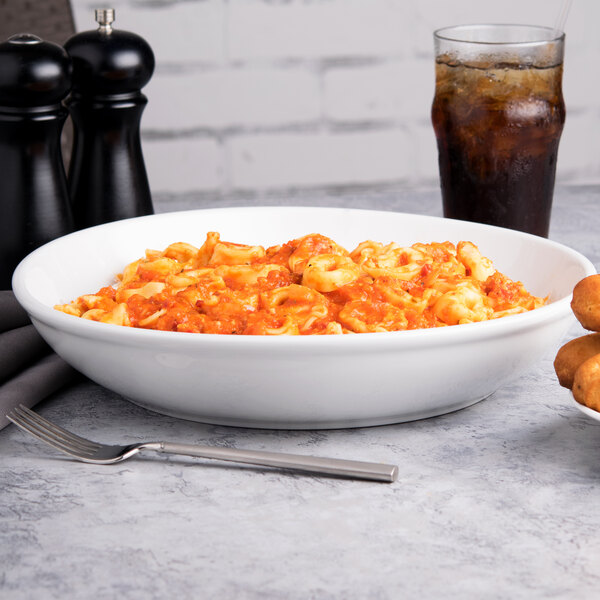 A Tuxton porcelain pasta bowl filled with pasta and a drink on a table.