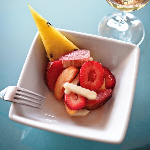 A Tuxton bright white square china bowl filled with fruit on a table with a fork.