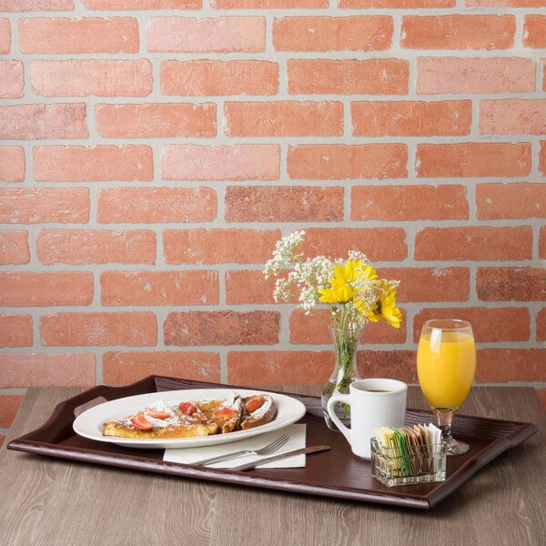 A mahogany room service tray with breakfast food, a plate of food, a glass of orange juice, and a vase of yellow and white flowers on it.