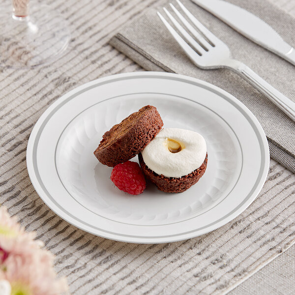 A WNA Comet white plastic plate with silver accent bands holding a brownie with white frosting and a raspberry.