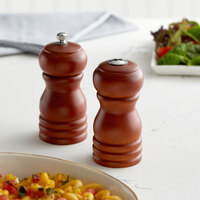 Short wooden salt shaker next to short wooden pepper mill on tabletop with pasta entree