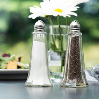 Clear glass salt and pepper shakers in front of daisies in vase with water