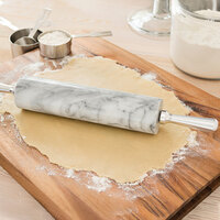 A marble rolling pin on rolled dough sitting on a cutting board.