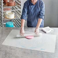 Someone rolling fondant out on a baking mat with a rolling pin.