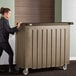 A woman pushing a Cambro Granite Sand and Cocoa Designer Series portable bar.