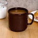 A brown GET plastic mug filled with a brown liquid on a wooden surface next to a plate of pastries.