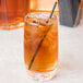 A Chef & Sommelier highball glass with brown liquid, ice, and a straw.