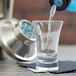 A close-up of clear liquid being poured into an Arcoroc shot glass.