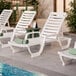 A white adjustable resin chaise lounge chair with a slatted design, positioned by a poolside.