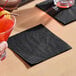 A black 2-ply beverage or cocktail napkin placed on a light wooden surface.