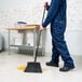 A warehouse broom with black unflagged bristles and a 48-inch handle being used to sweep debris on a tiled floor.
